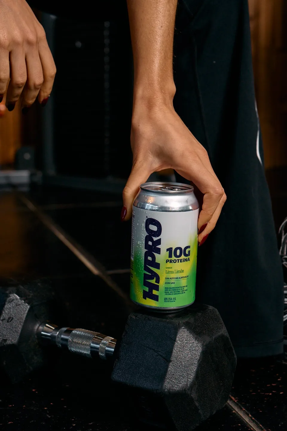 Mano tomando una lata de HYPRO apoyada sobre una mancuerna