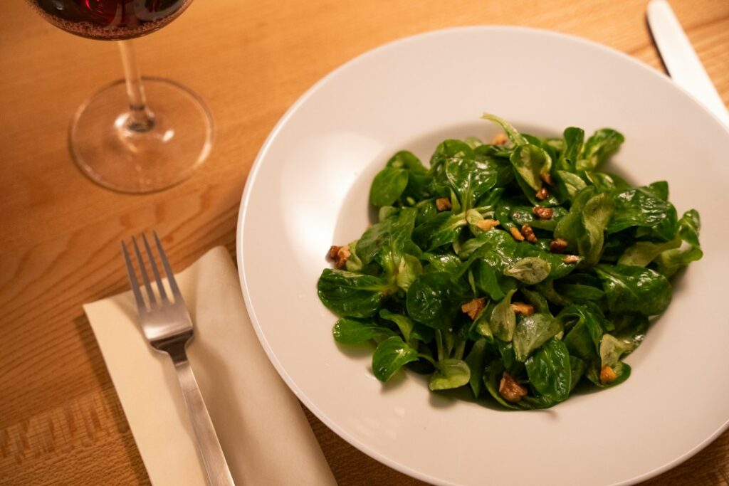 bowl of spinach salad with nuts and seeds on wooden table