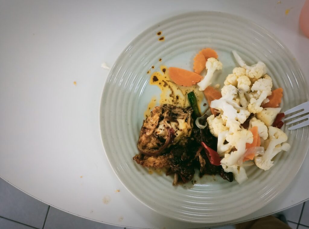 overhead view of a balanced meal plate with grilled chicken, vegetables and grains on a wooden table, natural daylight
